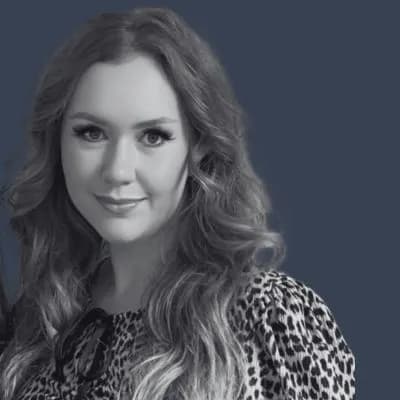 Woman with long, wavy hair and a leopard-print blouse poses against a dark blue background, smiling slightly.