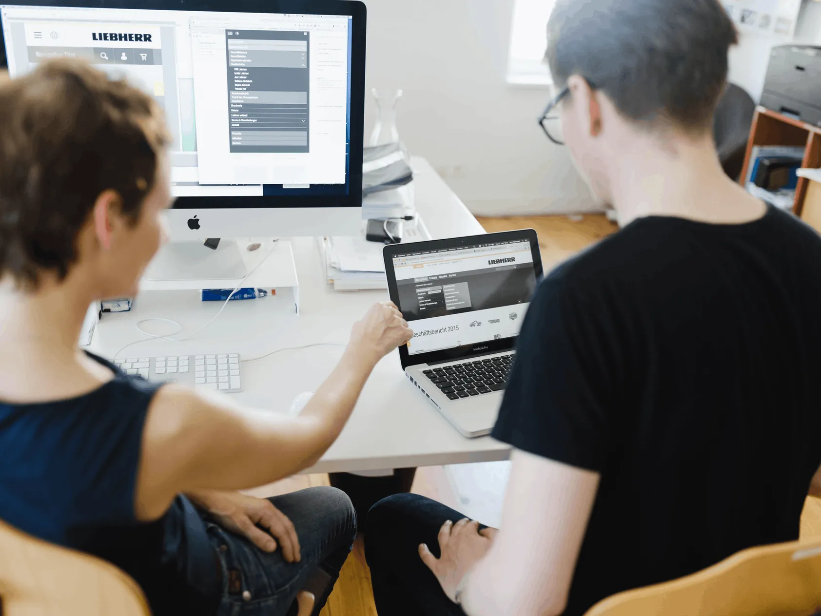 Zwei Personen arbeiten nebeneinander an Bildschirm und Laptop