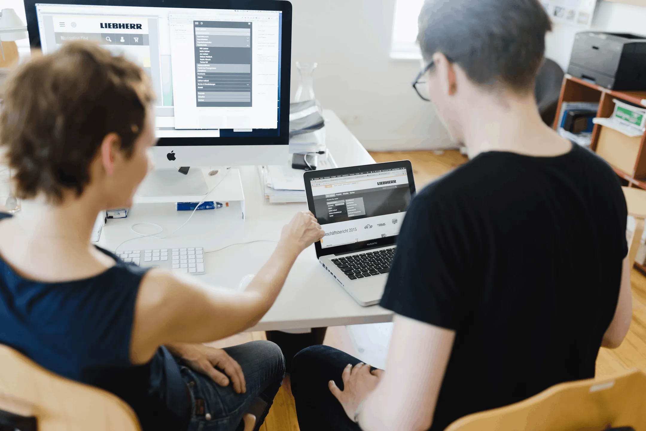 Zwei Personen arbeiten nebeneinander an Bildschirm und Laptop