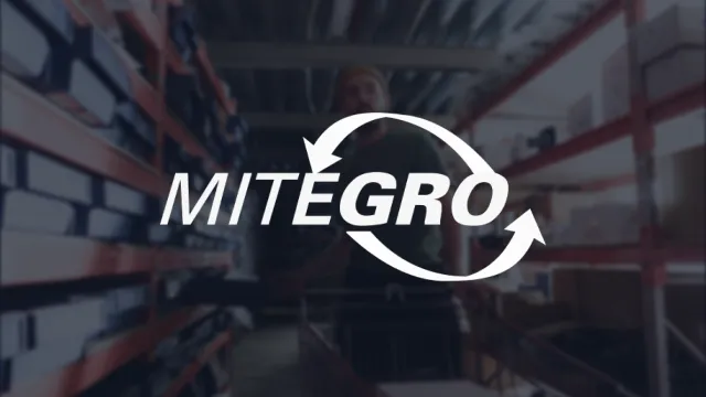 Text "MITEGRO" with circular arrows overlaying a blurred image of a warehouse with shelves and a person in the background.